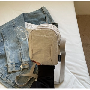 Vue détaillée du sac bandoulière en nylon beige à double zip sur fond de denim bleu classique