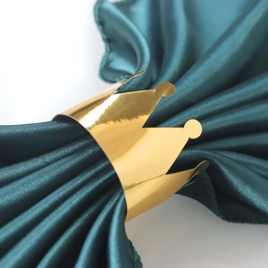 Macro shot of a shiny gold crown napkin ring on a dark green silk fabric background