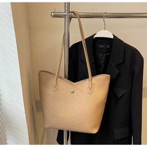 Detail of light khaki tote bag with litchi texture on a black blazer backdrop