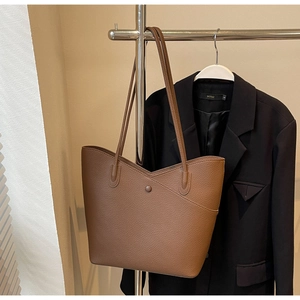 Detail view of large brown tote bag with V-shaped cut and litchi texture on garment rack