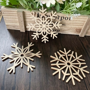 Three geometric laser-cut snowflake wooden coasters on a rustic dark wood tabletop