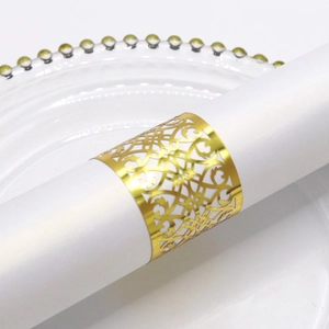 Macro detail of a hollow golden napkin ring with intricate vine patterns on white napkin