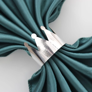 Detail of a silver crown napkin ring on teal silk fabric for elegant dining table decor