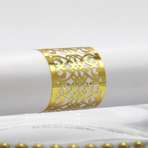 Close-up of laser-cut rose gold napkin ring with intricate hollow pattern on white linen
