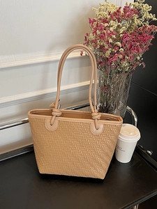 Woven khaki tote bag with knot handles and silver hardware shown in a lifestyle setting