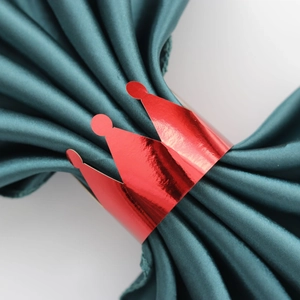 Close-up of a metallic red crown napkin ring on a dark green fabric napkin