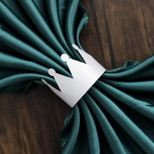 Macro shot of a silver crown-shaped paper napkin ring on a dark green satin fabric