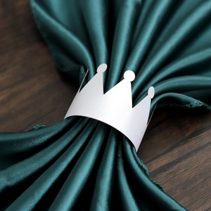 White crown paper napkin ring displayed on dark green satin fabric over wood table