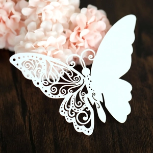 Detail of white laser cut butterfly place card with intricate hollow pattern on wood