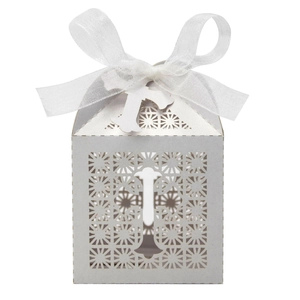 Detail of white laser-cut wedding favor box with organza bow and small cross pendant