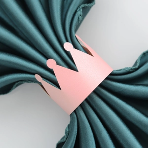Detail of pink crown paper napkin ring on green satin fabric for wedding table decor
