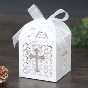 Detailed laser-cut white favor box with cross pattern and white ribbon bow on wood