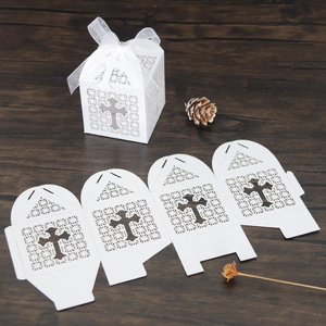 Macro detail of white laser-cut cross favor box with ribbon on wooden background