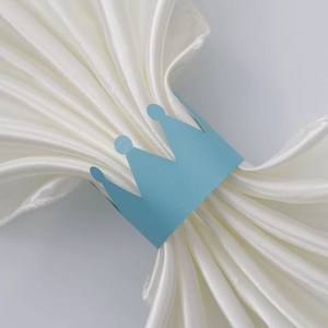 Detail of blue crown paper napkin ring on white satin fabric for wedding table decor