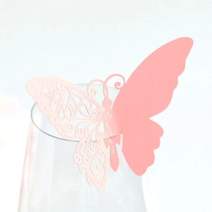 Pink laser-cut butterfly place card shown as a decorative topper on a clear glass rim