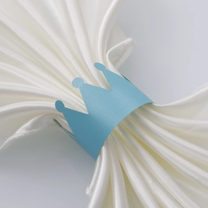 Close-up of light blue crown-shaped paper napkin ring on elegant white satin fabric