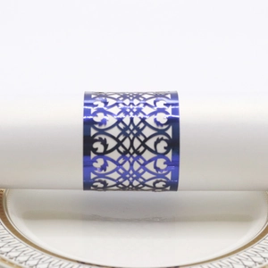 Detailed laser-cut blue metal napkin ring with geometric hollow patterns on white ceramic