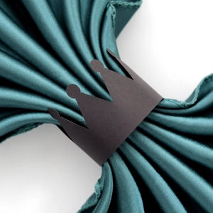 Detail of crown paper napkin ring in matte black on a dark green satin fabric