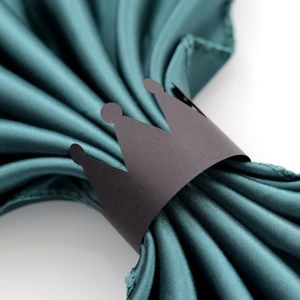 Detailed view of matte black crown paper napkin ring on dark green satin fabric texture