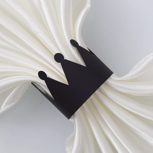 Detail shot of a black crown napkin ring on white silk cloth for party table setting