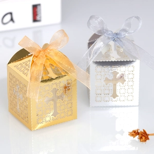 Detail of laser-cut cross pattern on gold and silver wedding favor boxes with ribbons