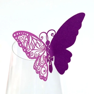 Macro shot of purple laser-cut butterfly paper card used as wine glass rim decoration