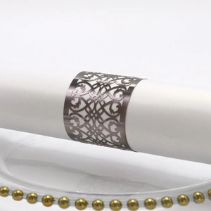 Close-up of a silver hollow laser-cut napkin ring with vine patterns on a napkin