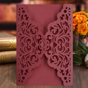 Detailed close-up of burgundy laser-cut invitation with intricate floral scroll patterns