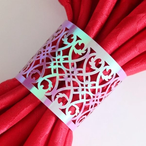 Macro detail of laser-cut iridescent napkin ring on a luxury red satin fabric