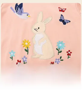 Detailed view of colorful rabbit and flower embroidery on soft pink cotton fabric