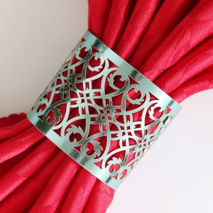 Elegant hollow metallic silver napkin ring with intricate vine patterns on red cloth