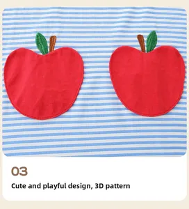 Détail d'appliqués de pommes rouges 3D avec broderie verte sur robe en coton rayé bleu