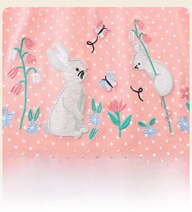 Détail du tissu rose à pois avec broderies délicates de lapins et de motifs floraux