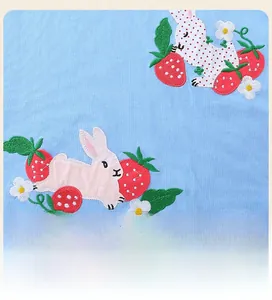 Détail de la broderie lapin et fraise sur un tissu en coton tricoté bleu clair