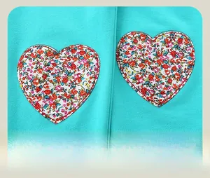 Detail of blue textured joggers featuring two symmetric floral heart patches with red stitching