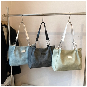 Three large tote bags in blue, grey, and green with chain straps on a metal rack