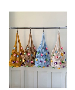 Detail of four colorful crochet tote bags with 3D floral accents on a hanging rack