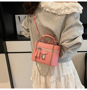 Detail of pink lychee leather box bag with metal chain strap worn by a model