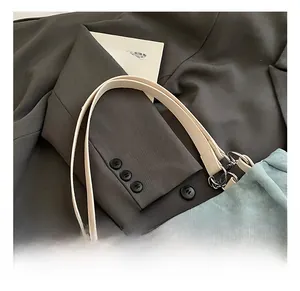 Detail of light blue corduroy tote bag with ivory straps and brand patch on gray blazer