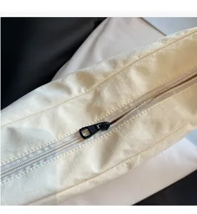 Detailed close-up of smooth black metal zipper closure on off-white nylon dumpling bag