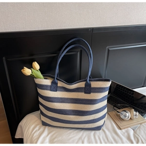 Détail du sac fourre-tout tissé à rayures bleues et blanches avec deux bretelles sur le lit