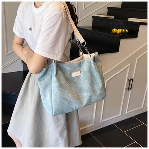 Detail of light blue corduroy tote bag with wide white strap and metal chain accents