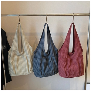 Three plaid canvas tote bags in white, blue, and red hanging on metal rack detail view