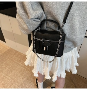 Detail of a black pebbled leather box bag with silver chain and padlock on a model