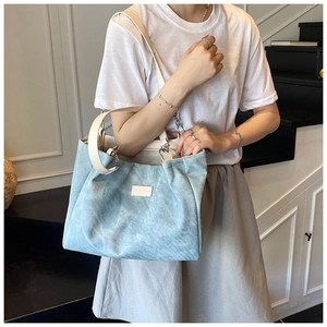 Detail of light blue corduroy tote bag with fashion label and beige synthetic leather straps