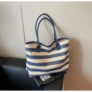 Détail du sac cabas tissé à rayures bleues et blanches avec fines anses sur canapé