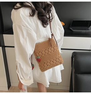 Detail of hand-woven straw shoulder bag with cute red strawberry charm accessory