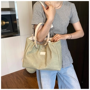 Detail of sage green canvas tote bag featuring white leather handles and chain strap
