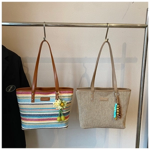 Detail view of large straw tote bags with colorful stripes and tassel charms on a rack