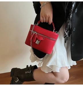 Detail of red box bag with lychee texture and metal chain held by fashion model